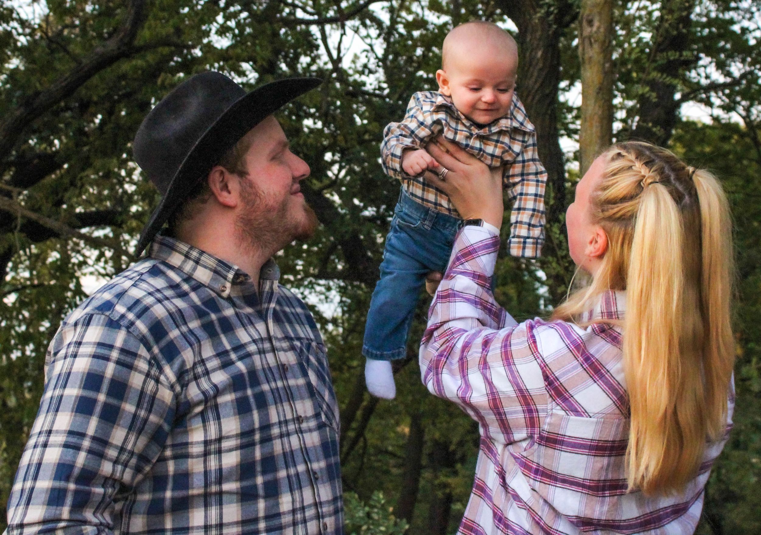 Family wearing plaid shirts embracing in autumn forest setting.
