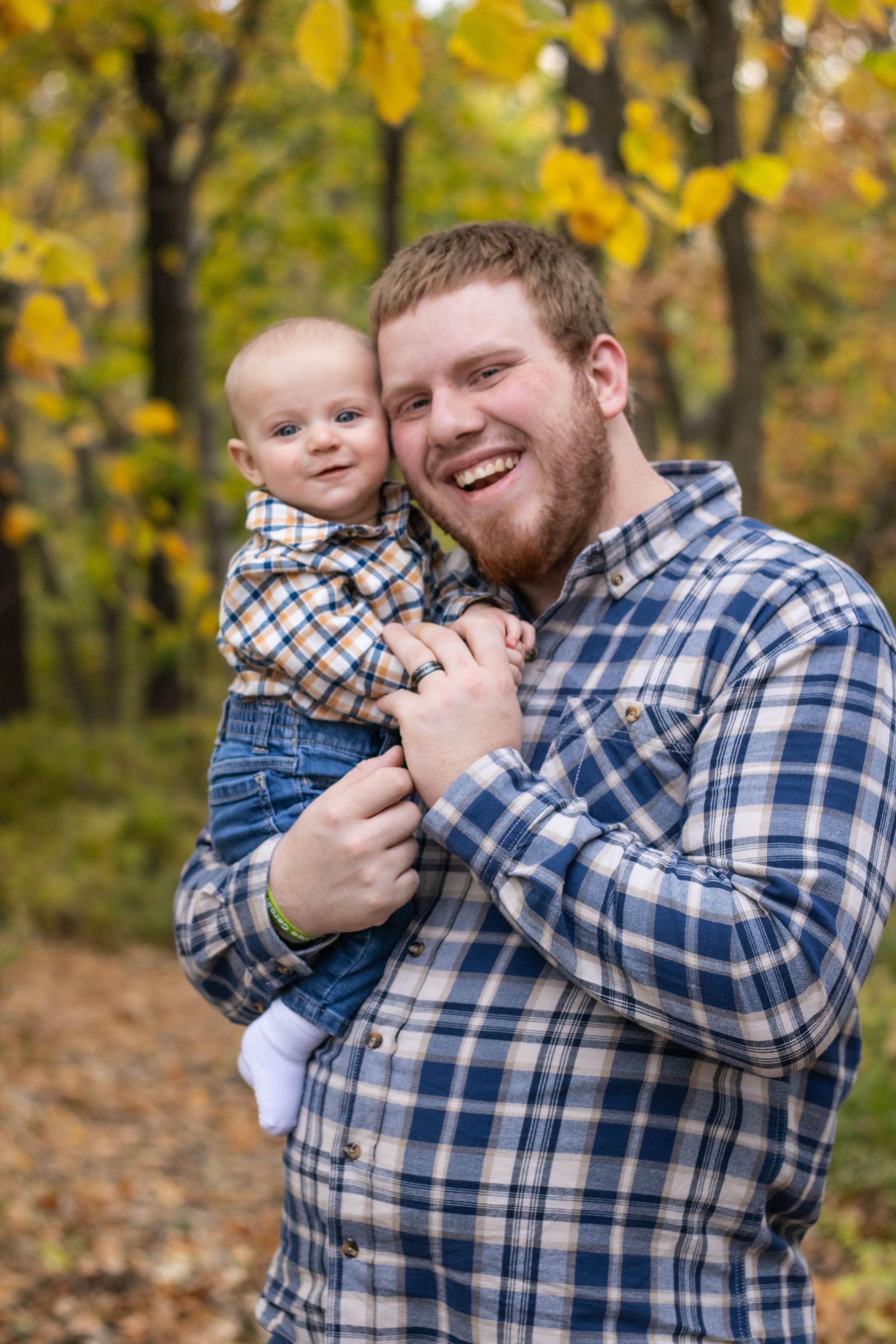 Family members share tender moment in wooded area with autumn colors.