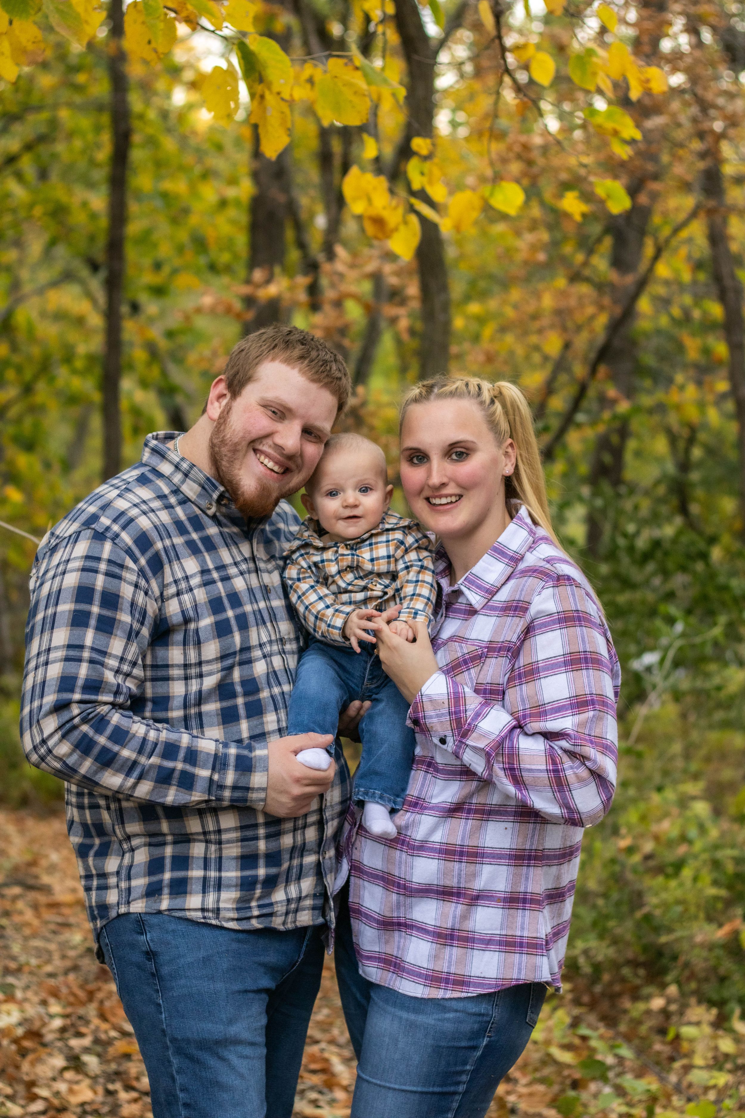 Family wearing matching plaid shirts poses together in fall forest setting.