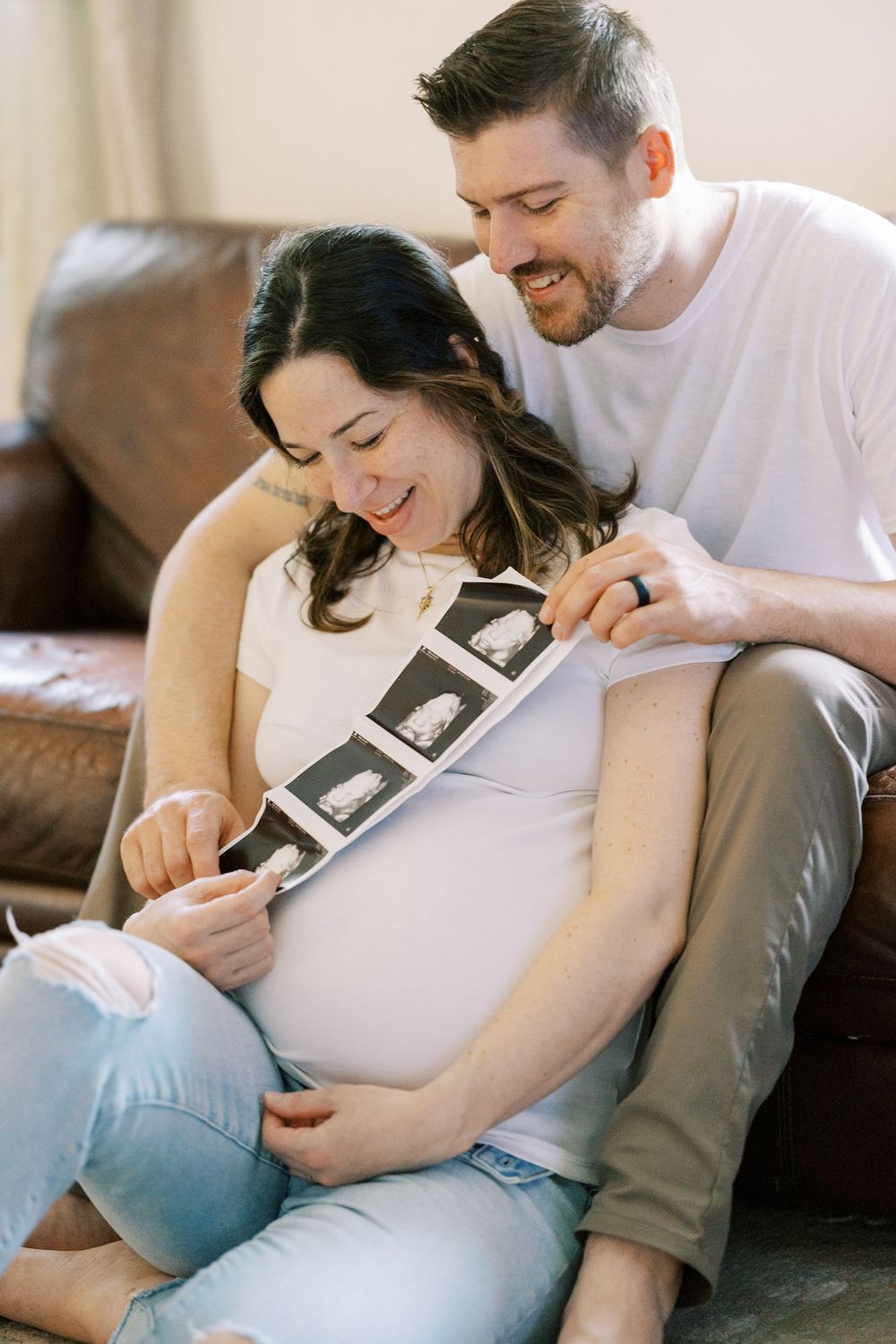 Expecting couple sharing joyful moment while looking at ultrasound photos on couch in Clifton, New Jersey.