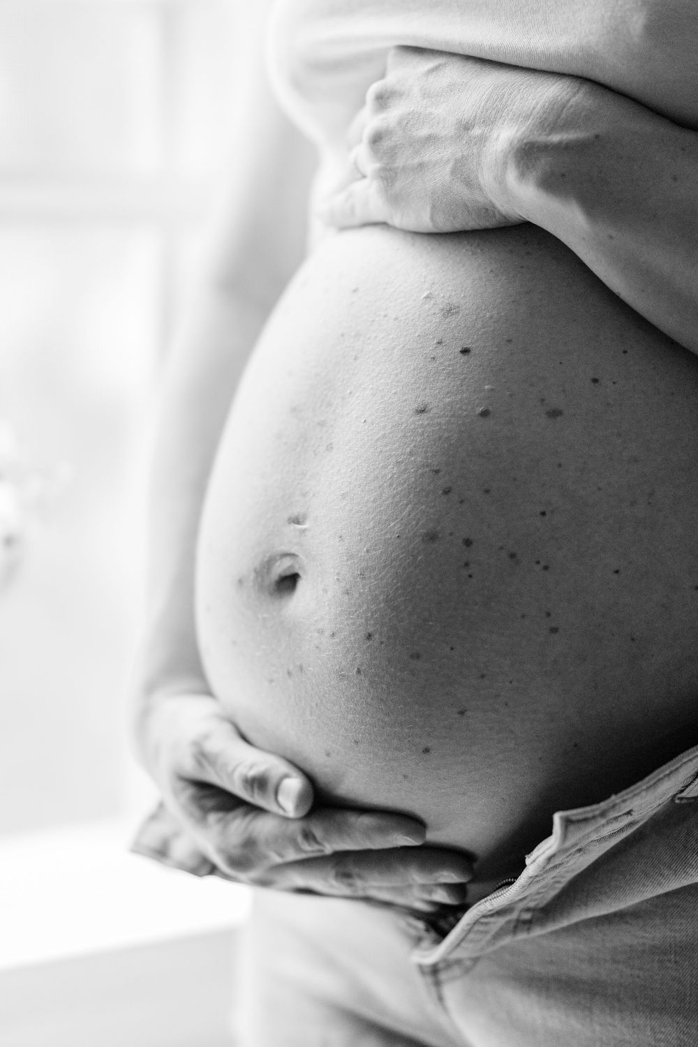 Black and white photo of a pregnant belly being cradled by hands in Clifton, New Jersey.