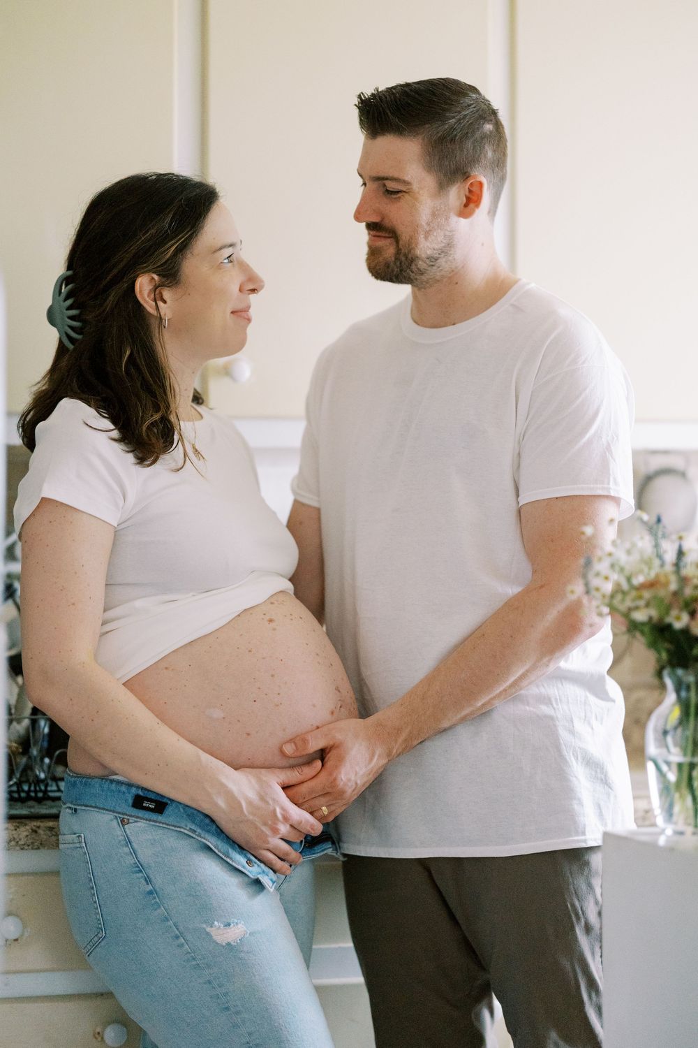 A tender moment between an expectant couple in white shirts and jeans in Clifton, New Jersey.