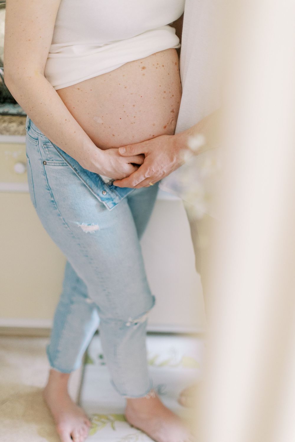 Pregnant belly shown in profile with hands gently resting on the bump in Clifton, New Jersey.