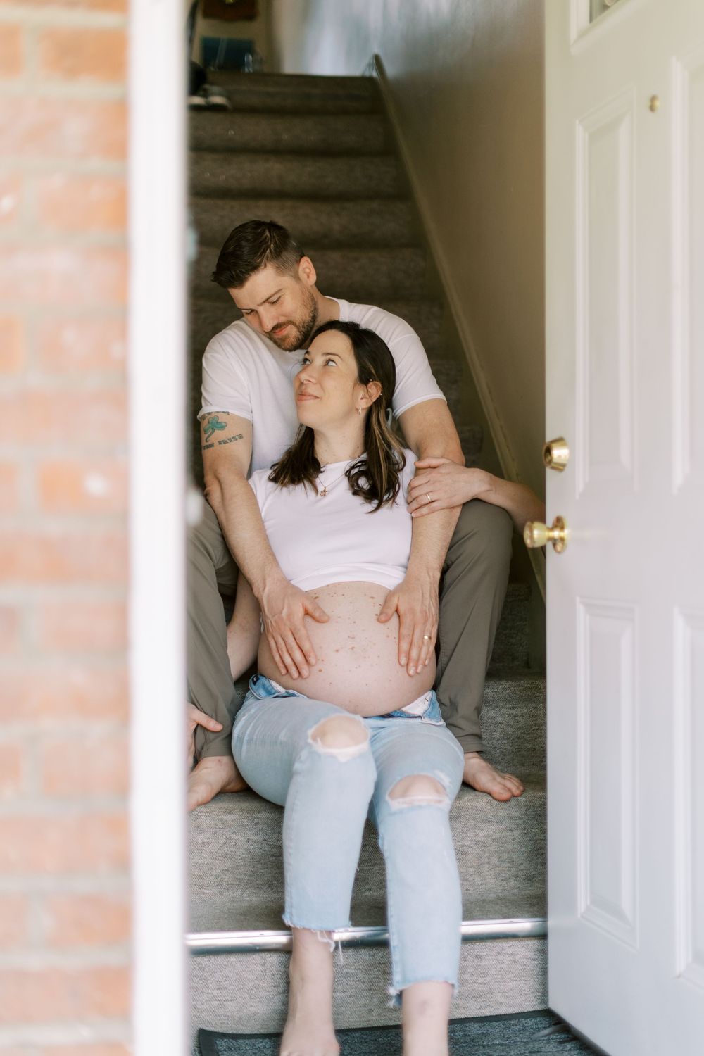 An expecting couple sharing an intimate moment on carpeted stairs in Clifton, New Jersey.
