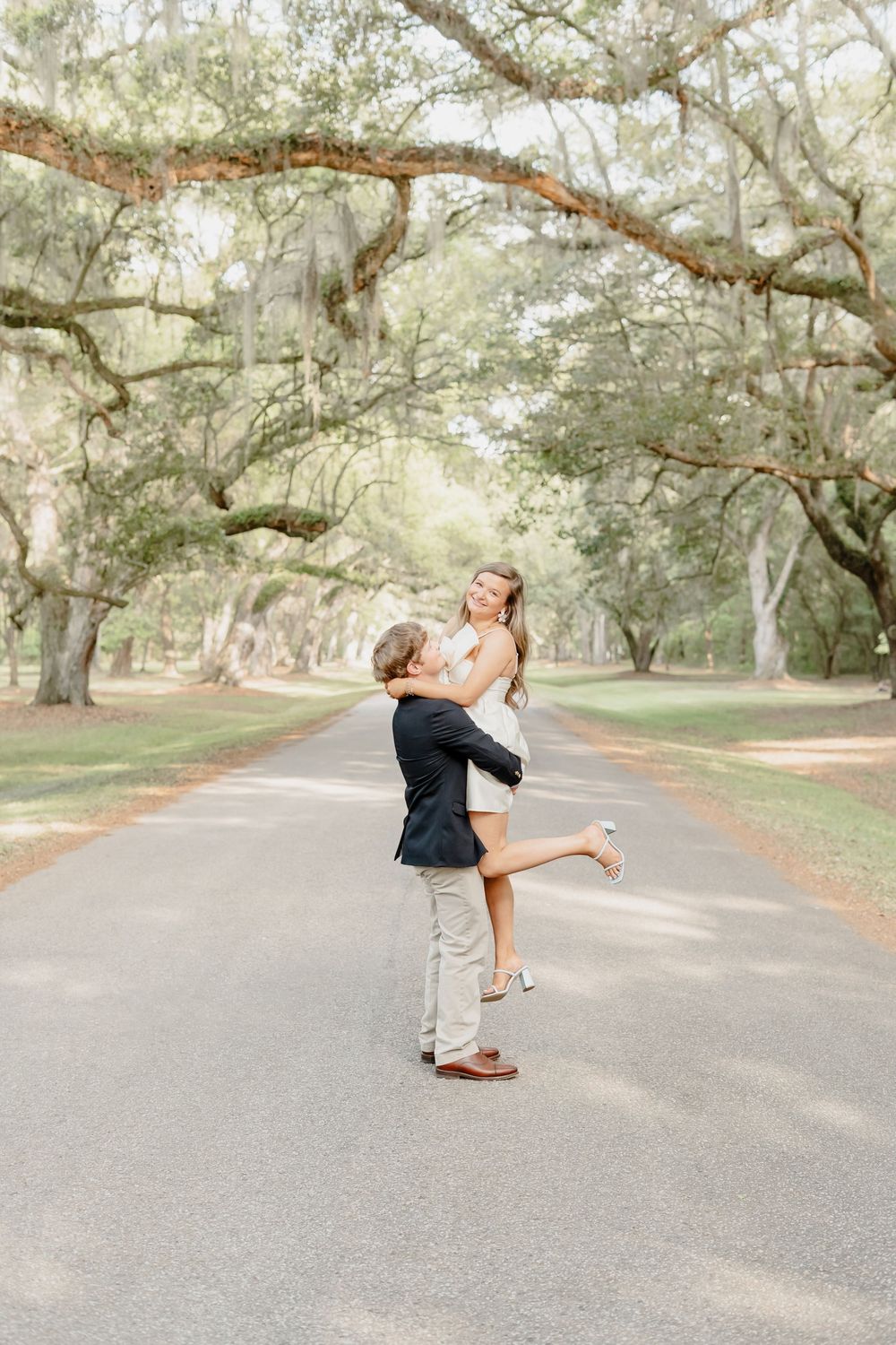 A romantic embrace under Spanish moss draped trees on a serene tree-lined road.