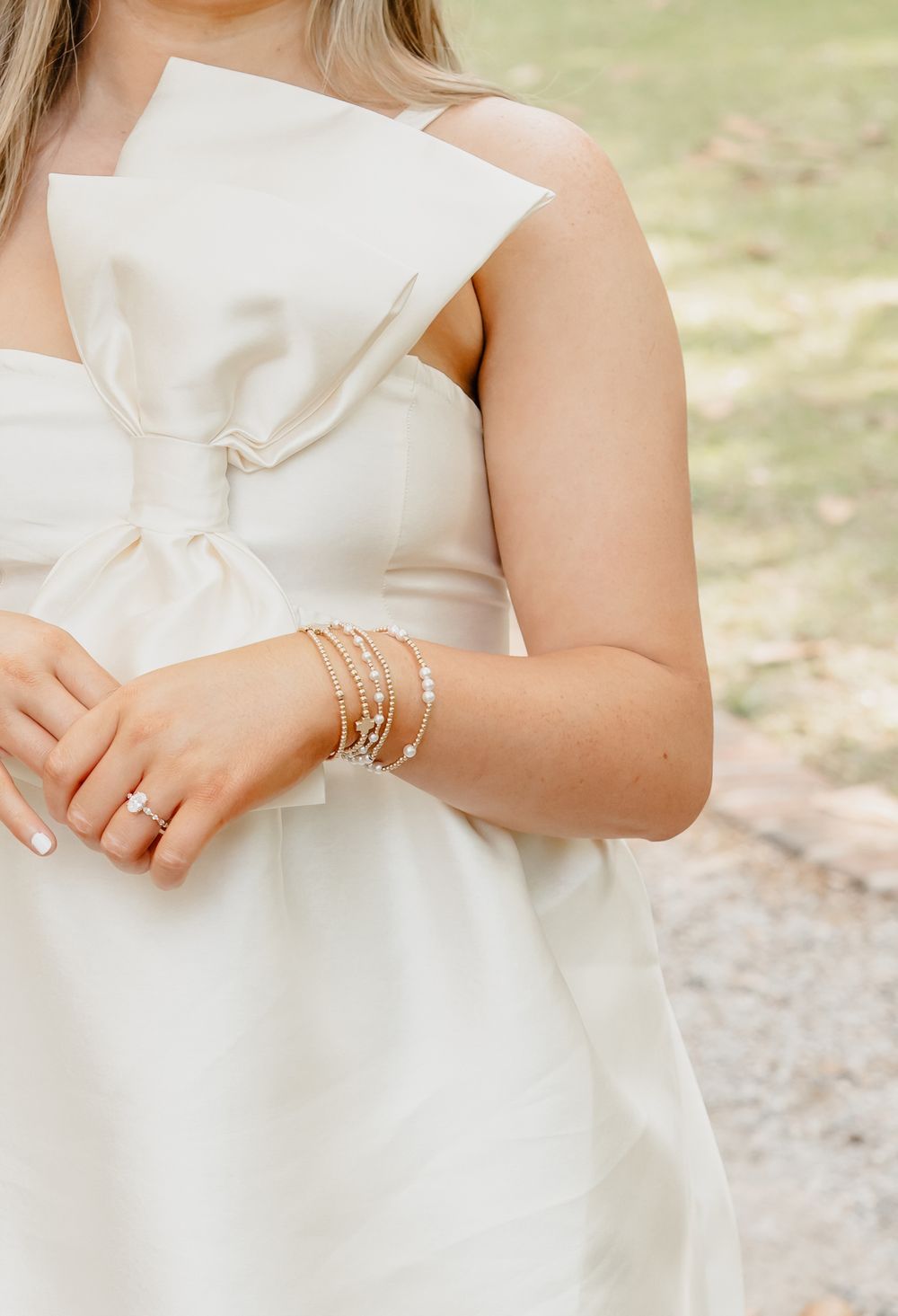 Close-up of delicate pearl and crystal bracelets adorning a wrist against a white dress with bow detail.