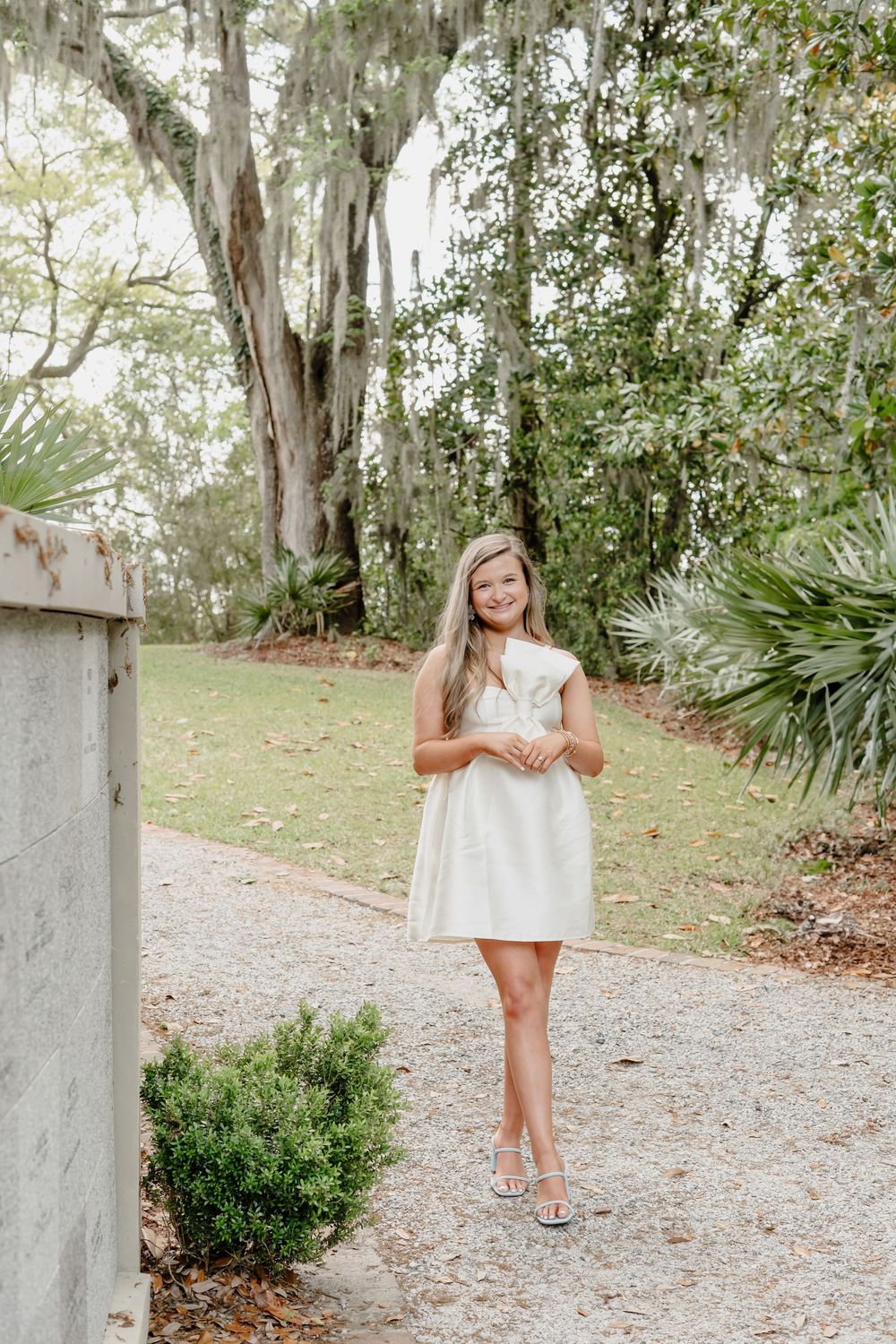 White lace dress and sandals photographed on a garden path with Spanish moss draped trees and tropical plants in background.