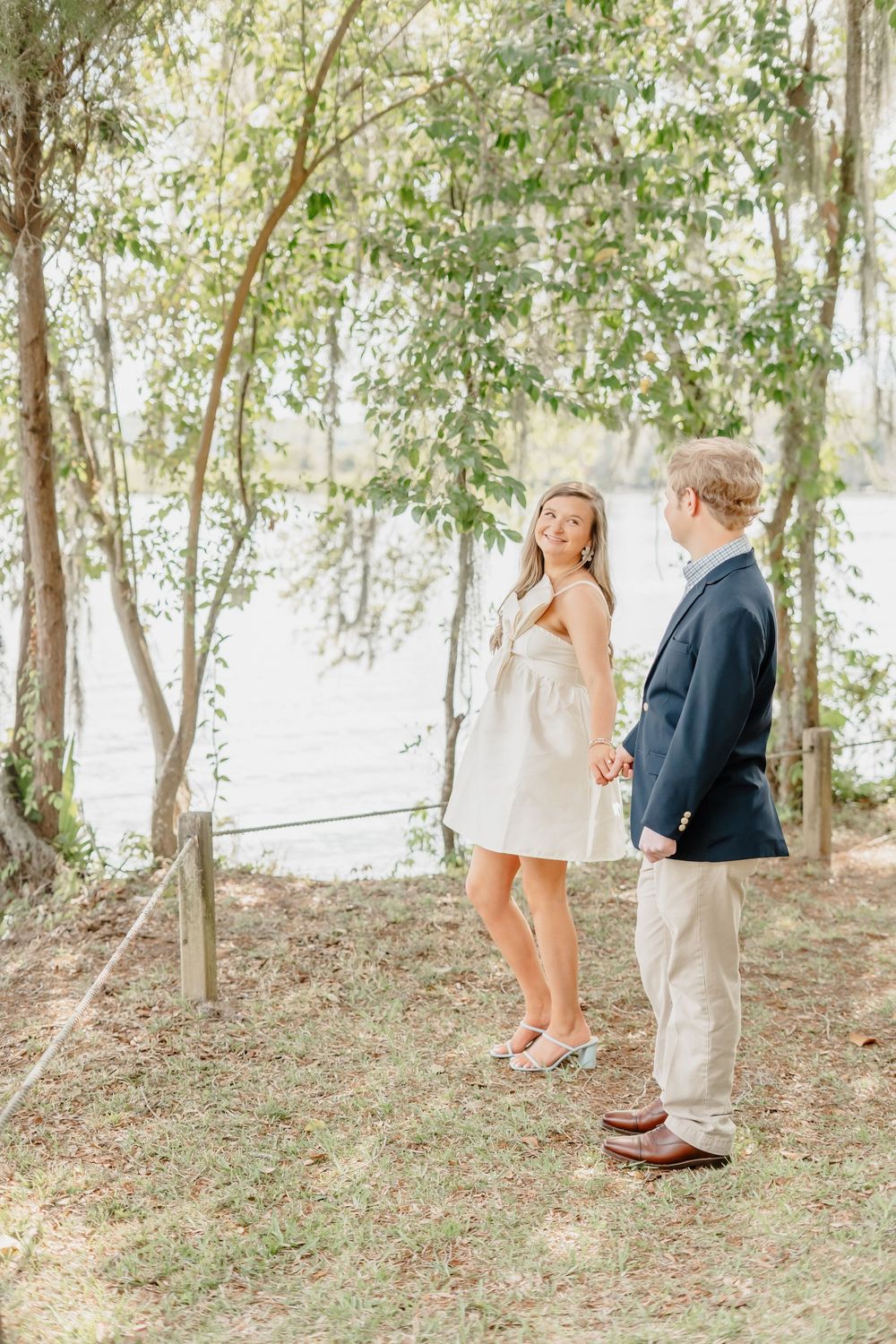 Couple stands together in romantic woodland setting with birch trees and filtered sunlight.