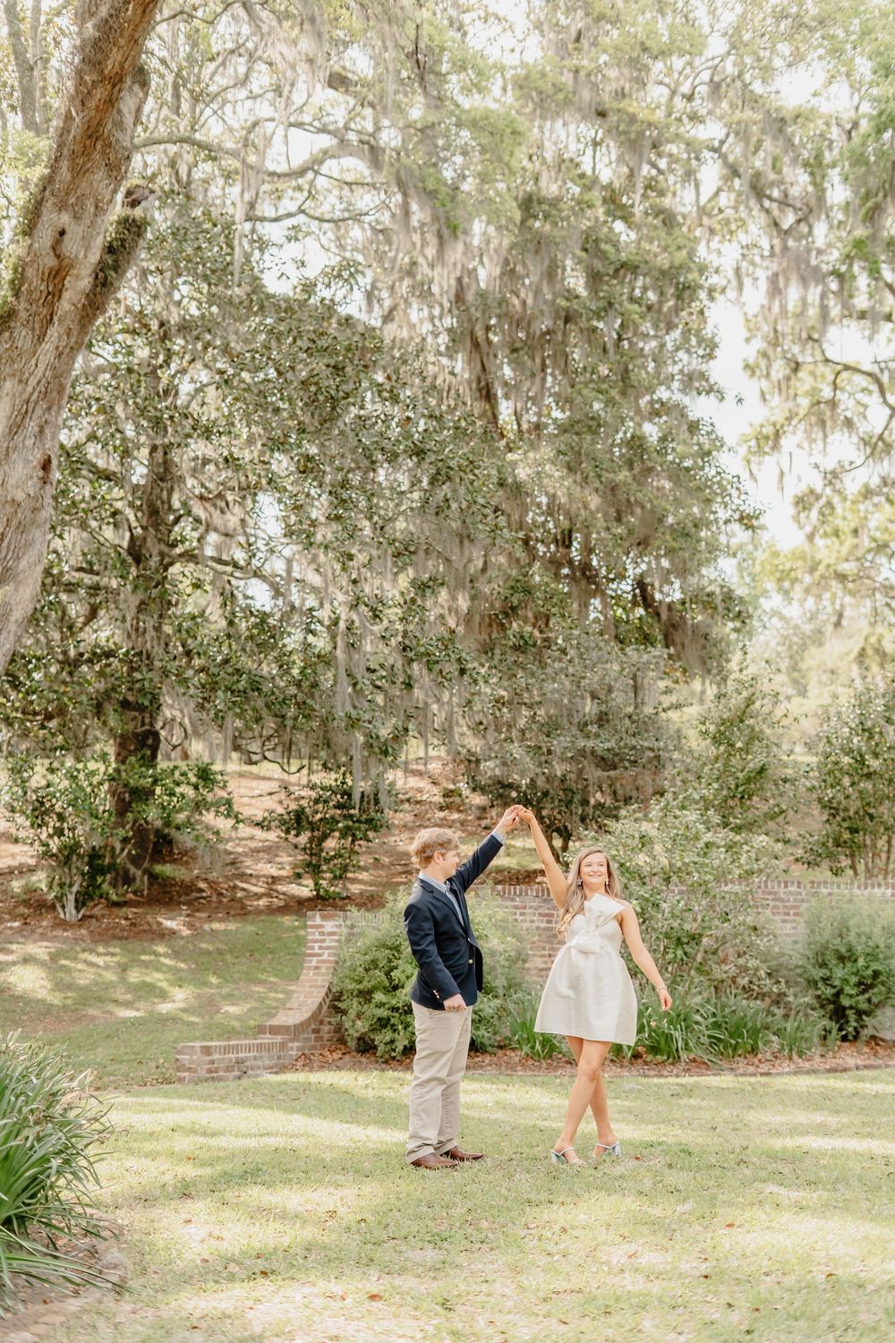 A couple dances together under Spanish moss-draped trees in a romantic garden setting.