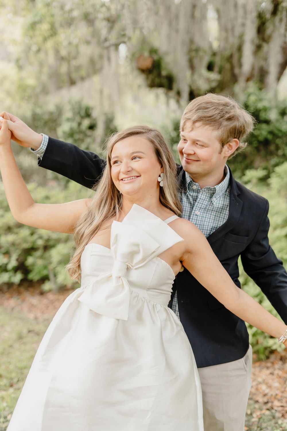 Couple in a garden setting enjoying a romantic dance moment under Spanish moss with a white dress and dark blazer.
