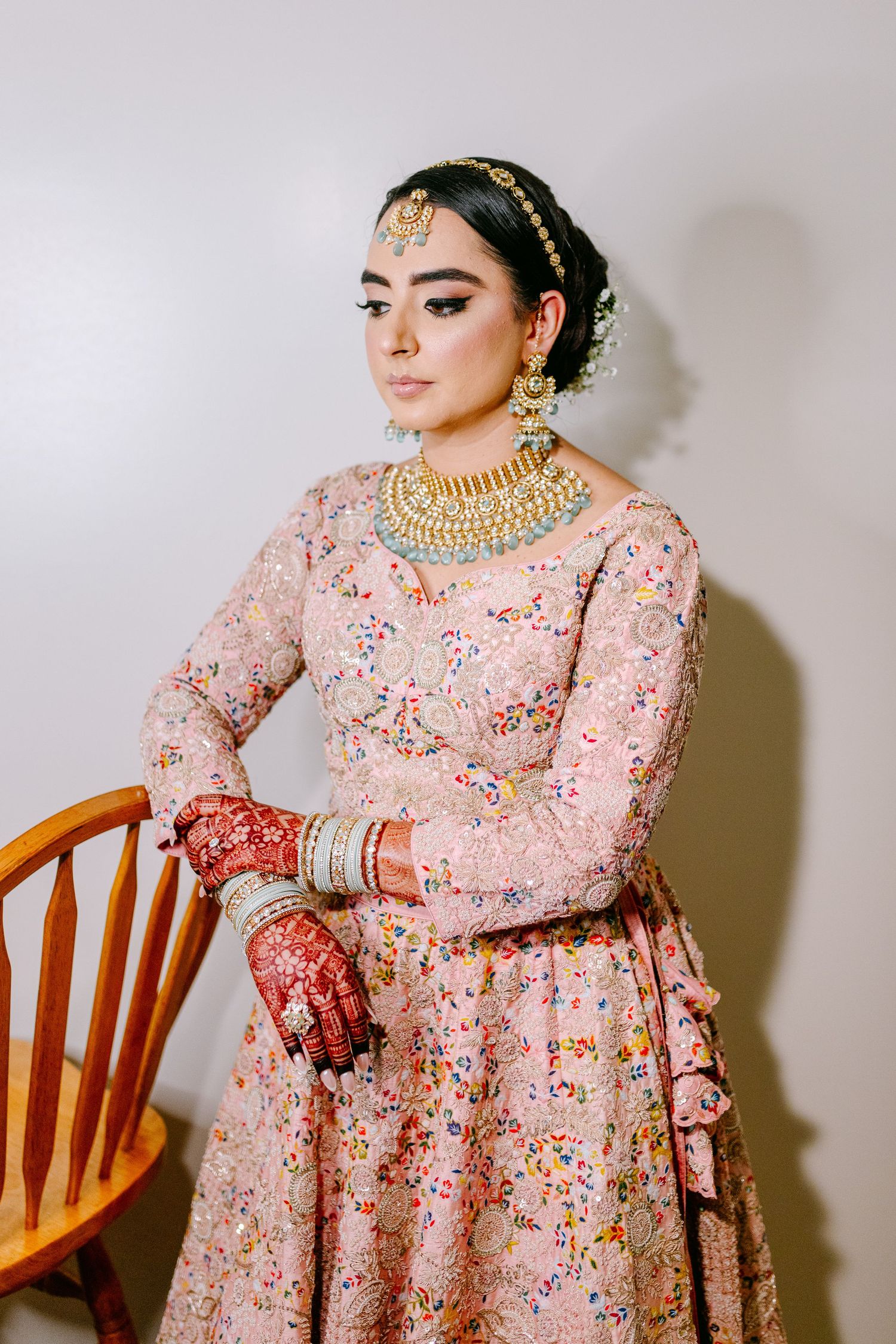 South Asian bride in pink floral lehenga with traditional gold jewelry and makeup.