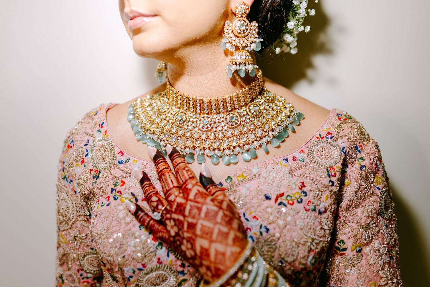 Detailed shot of Indian bridal jewelry and henna adorned hands with pink floral outfit.