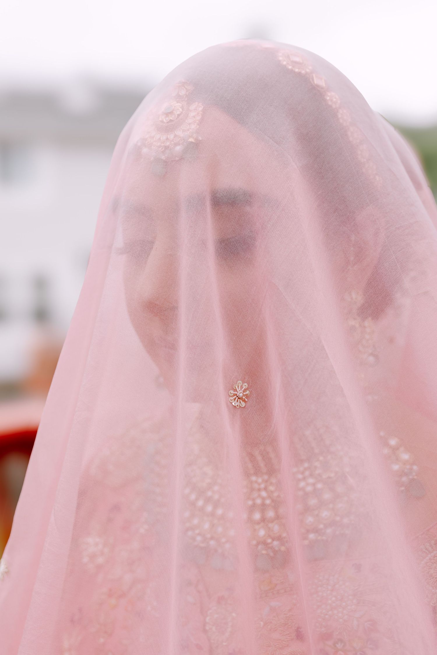 Bride in traditional South Asian attire wearing pink veil with delicate embroidery details.