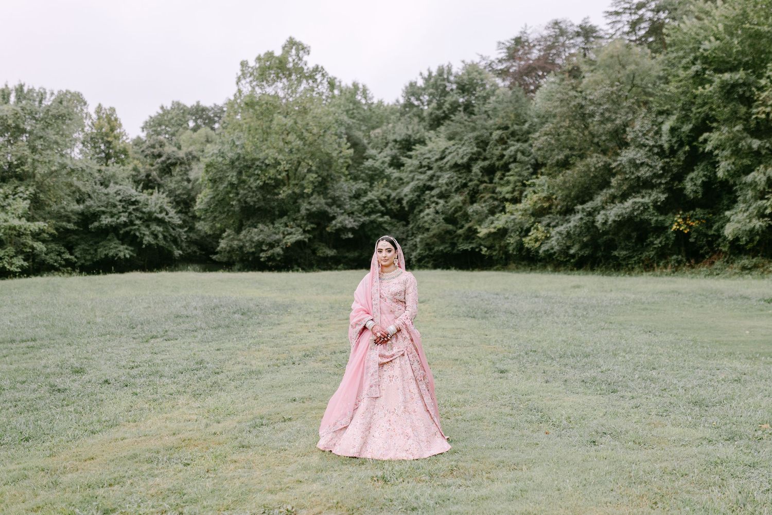 Bride in pink lehenga standing alone in a peaceful garden setting.