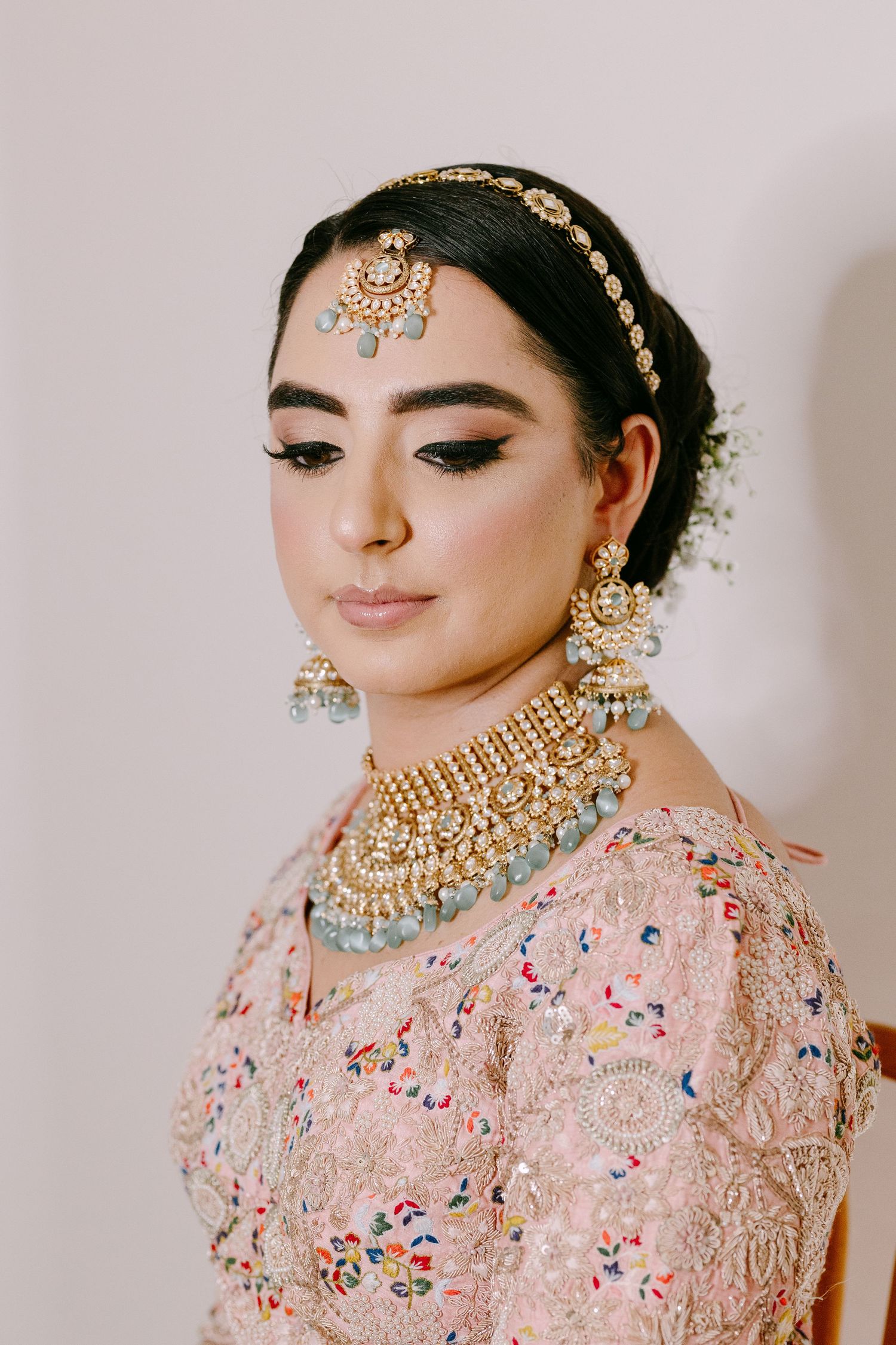 Traditional South Asian bridal look with ornate gold jewelry and pink embroidered outfit.