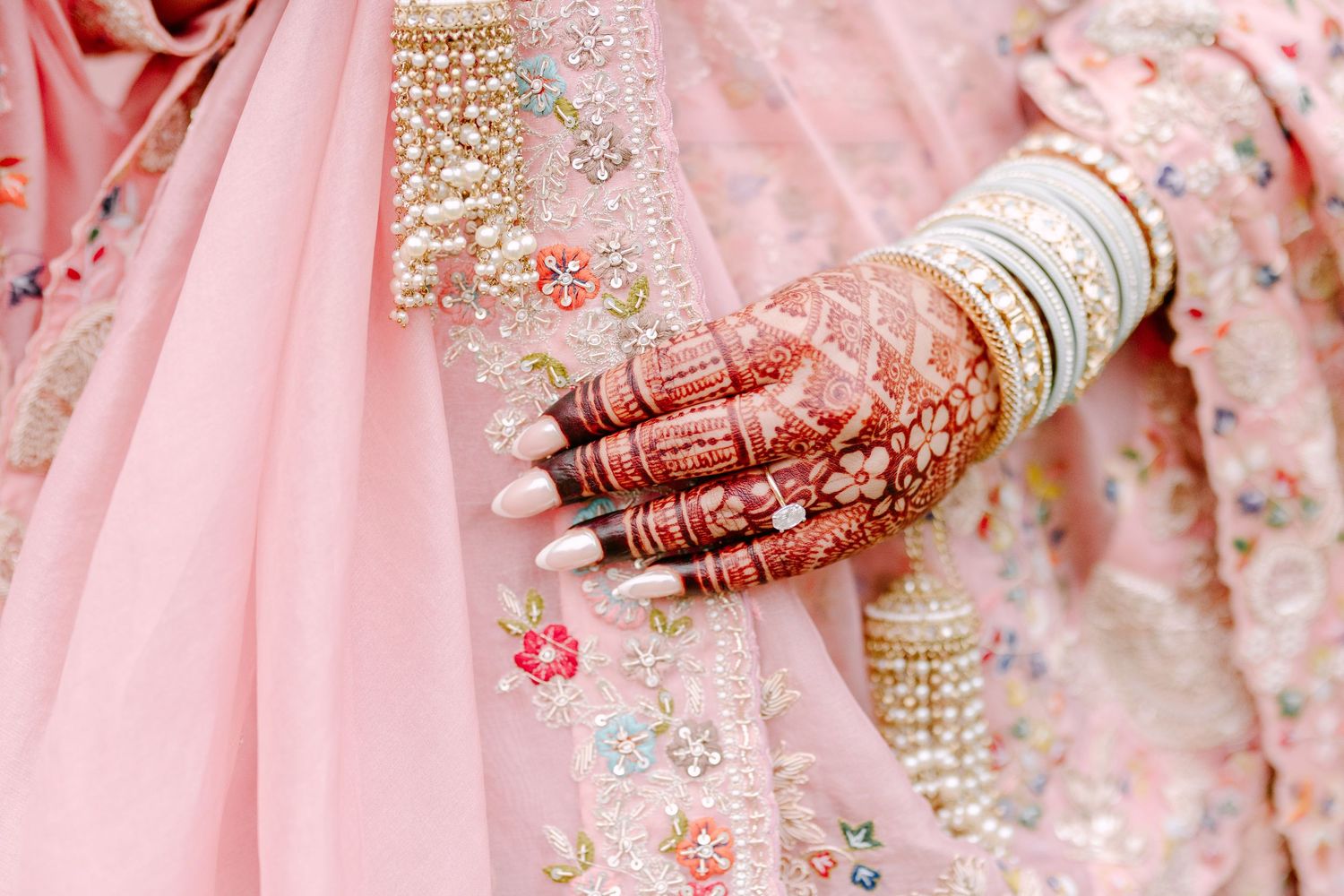 Close-up of henna-adorned hands with white bangles against pink embroidered fabric.