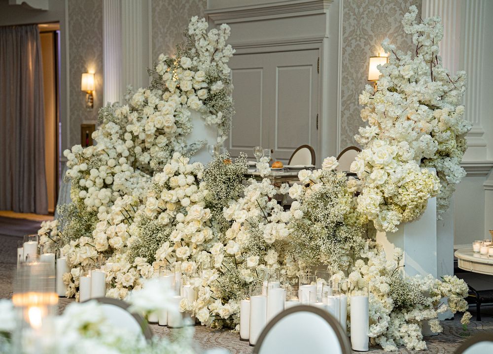 Elegant white floral arrangements with hydrangeas and roses decorate a luxurious interior space with warm lighting.