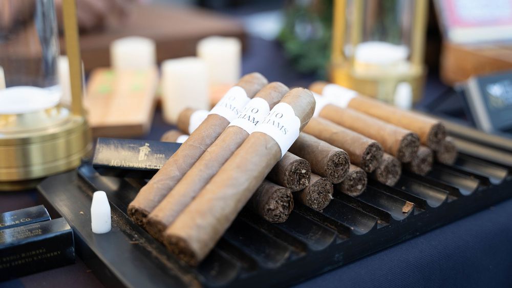A row of premium hand-rolled cigars displayed on a wooden surface with soft lighting and blurred background.