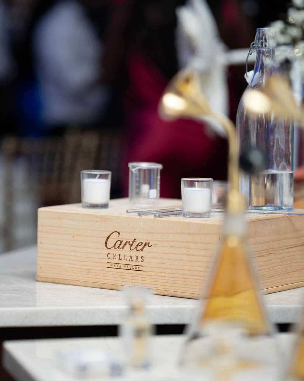 A wooden Cartier Cellars display box with candles and wine bottles arranged on a table at a tasting event.