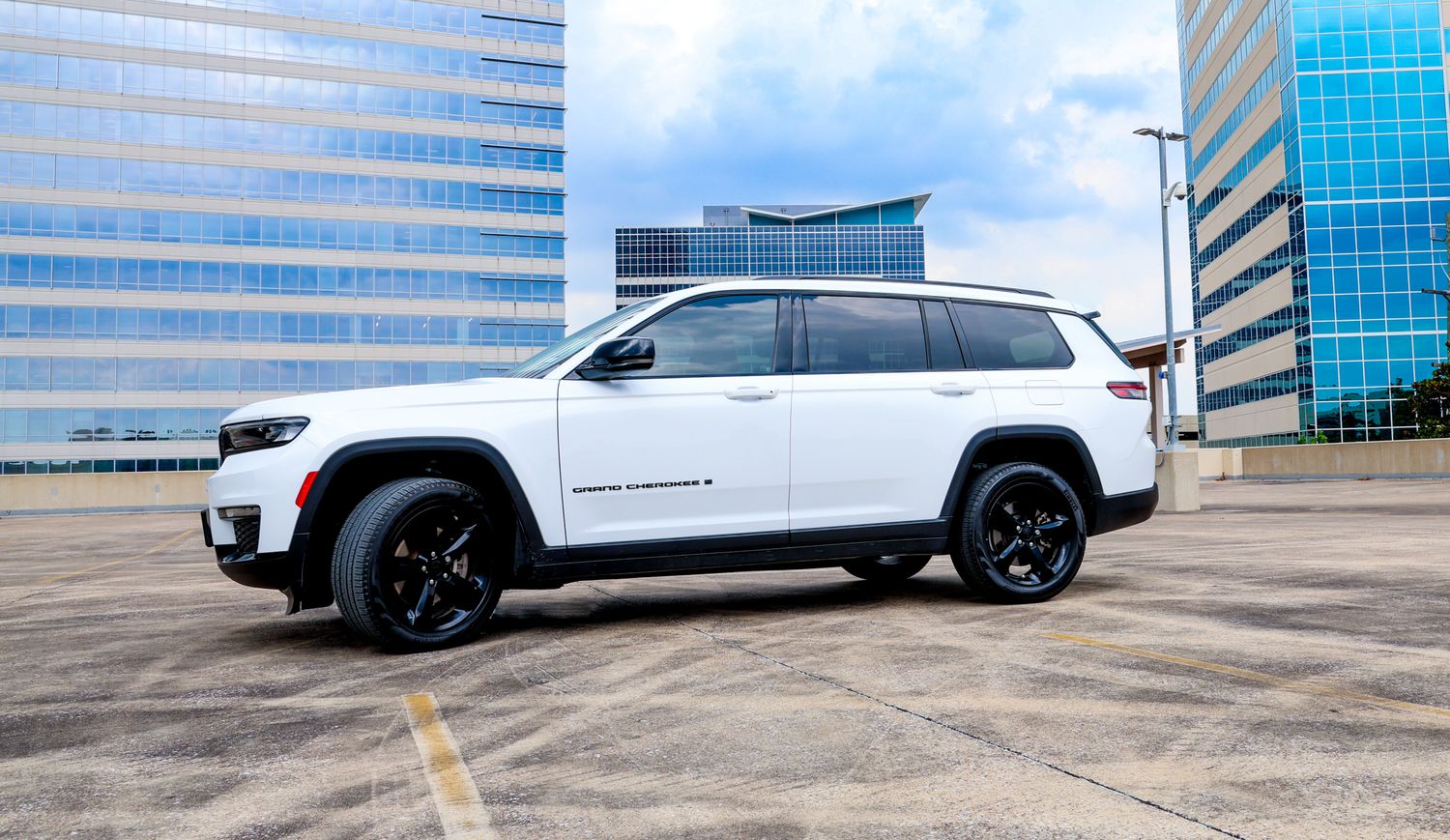 Modern white SUVs parked in front of glass office building with reflective windows.