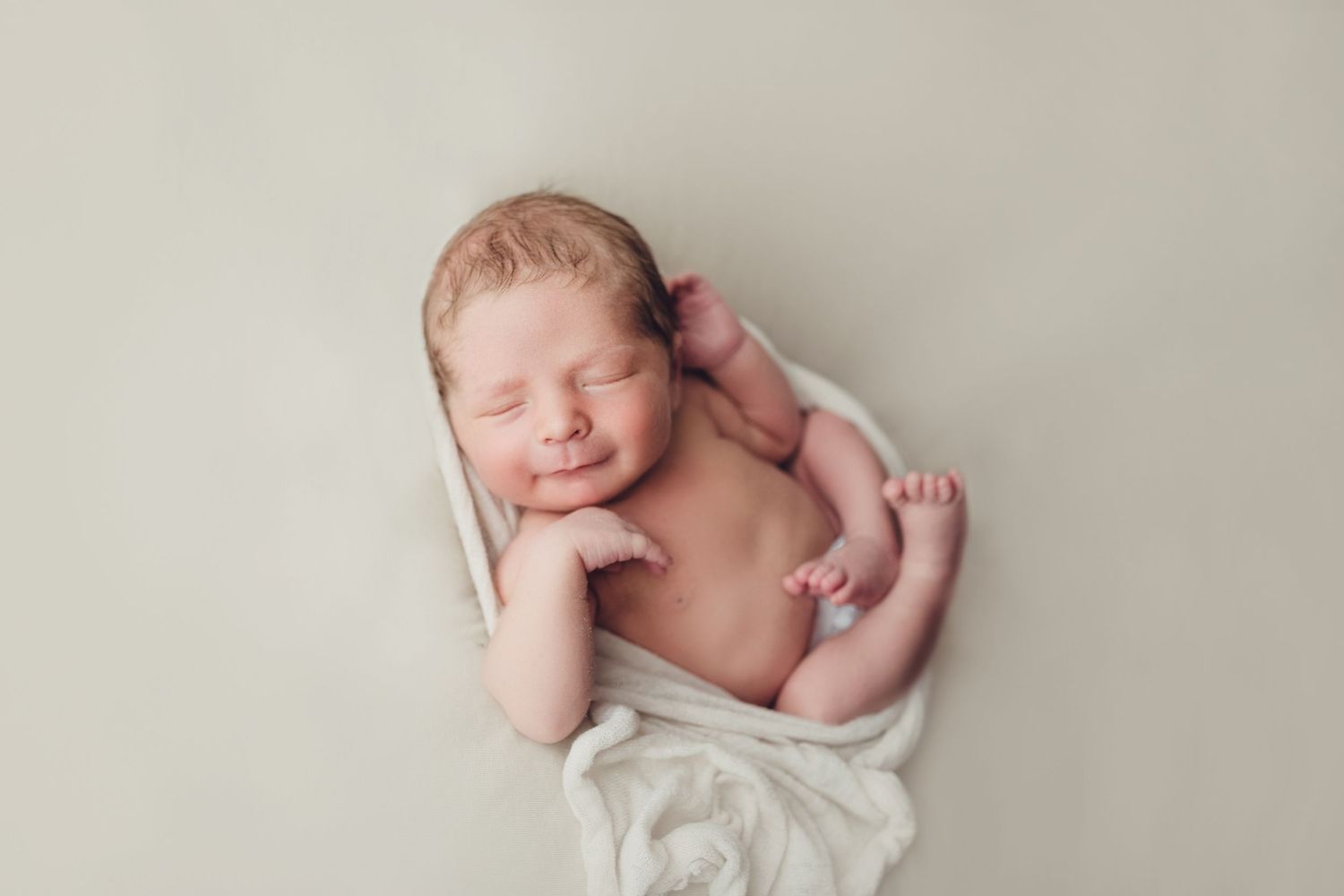 Peaceful sleeping newborn wrapped in white fabric on neutral background.