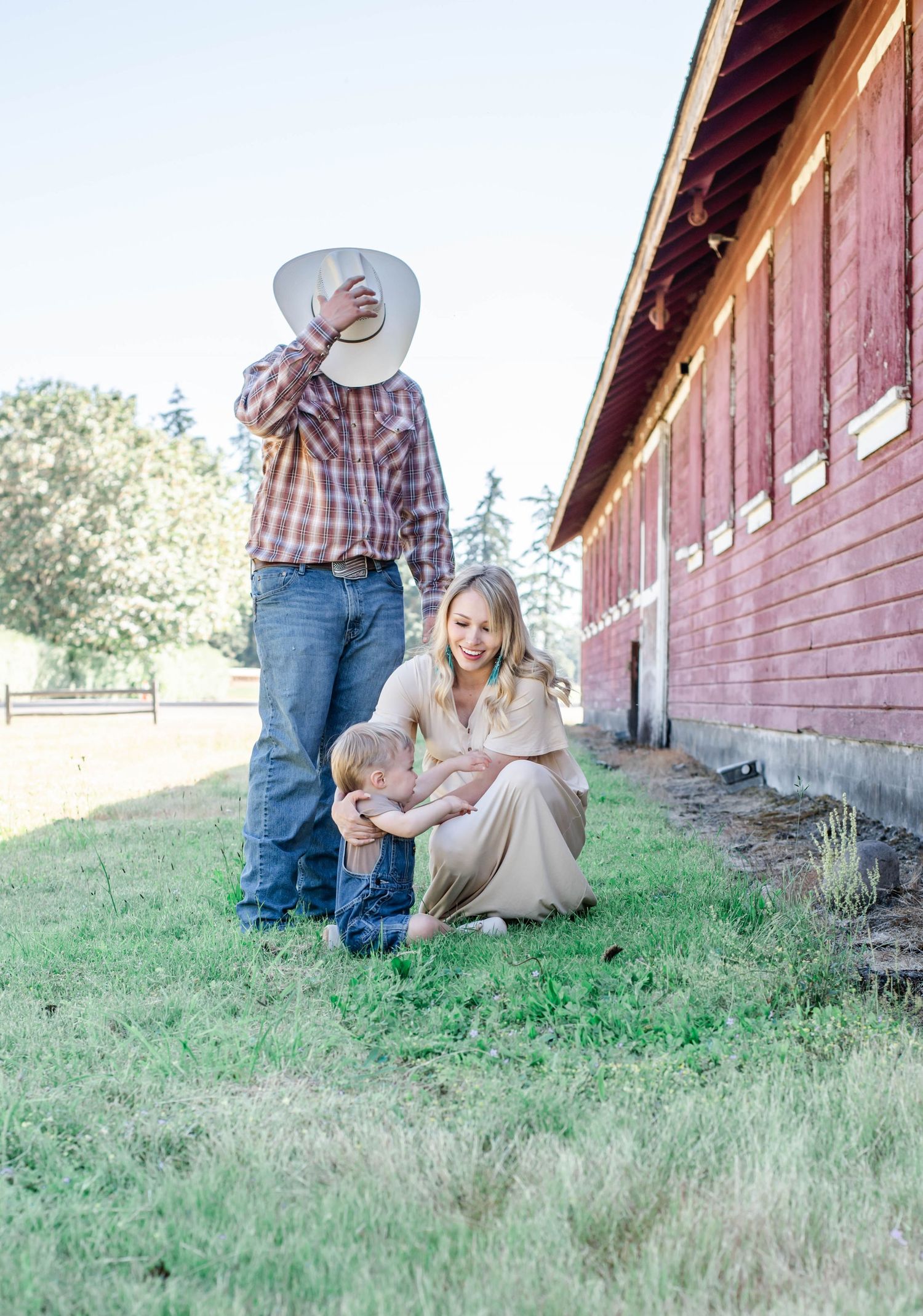 Sweet family moments photographed beside a vintage red barn in casual western wear.