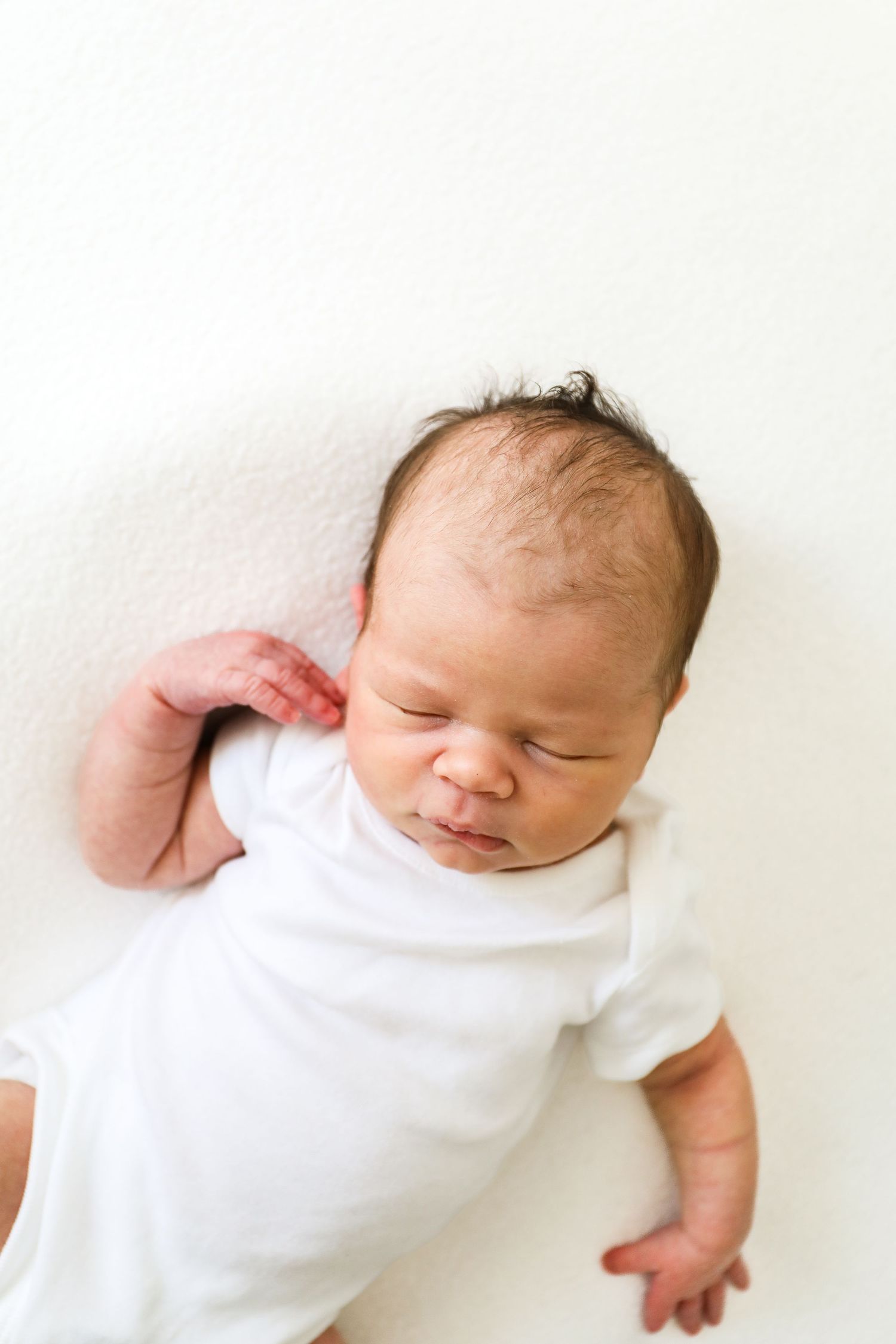 Newborn baby wearing white onesie sleeping peacefully on white background, during newborn shoot in Nottingham