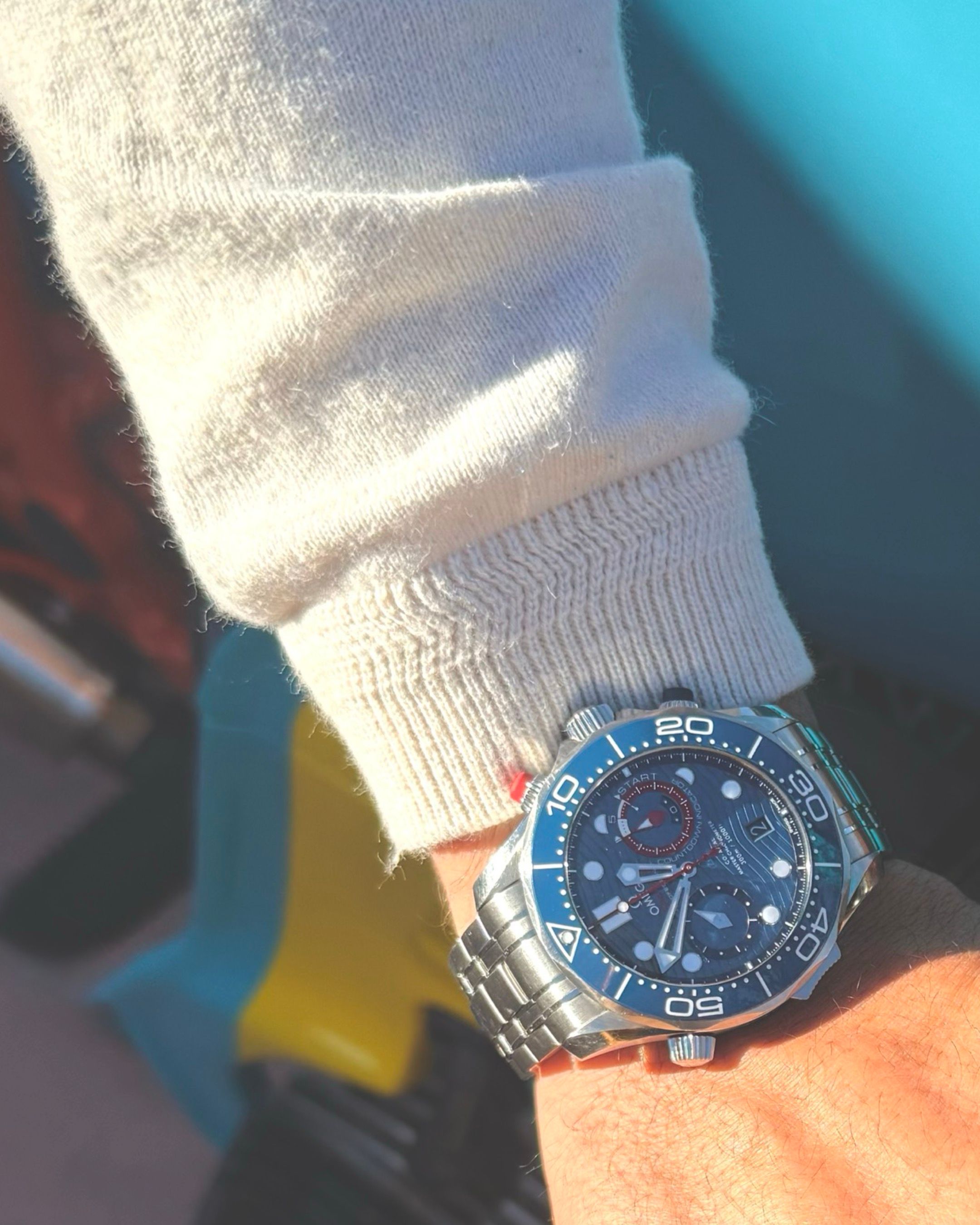 Close-up of a blue diving watch worn with a white sweater sleeve.
