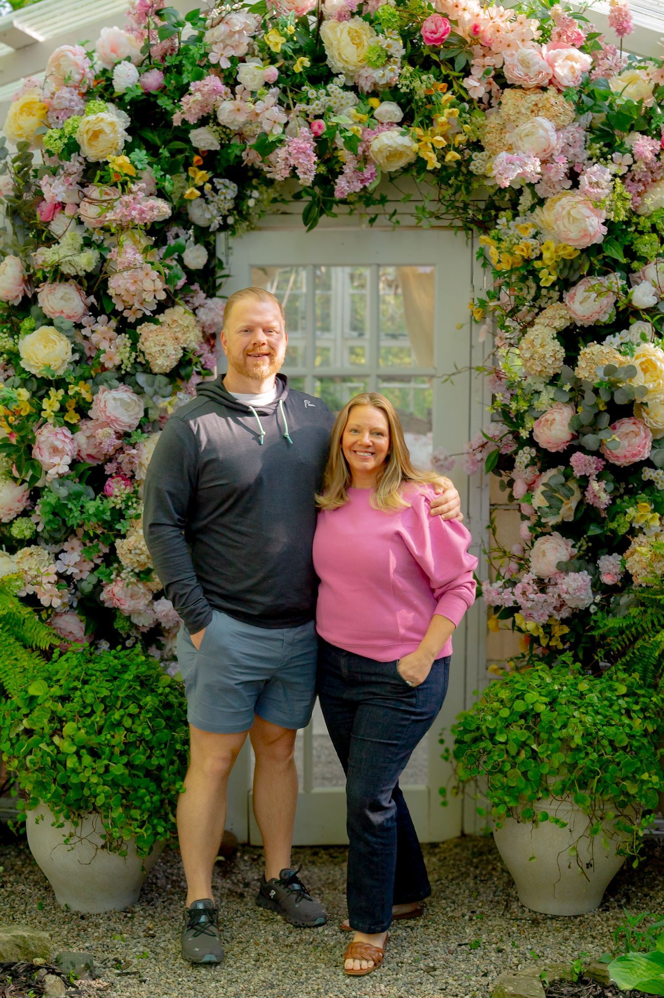Beautiful floral arch with pink and white roses frames a garden entrance.