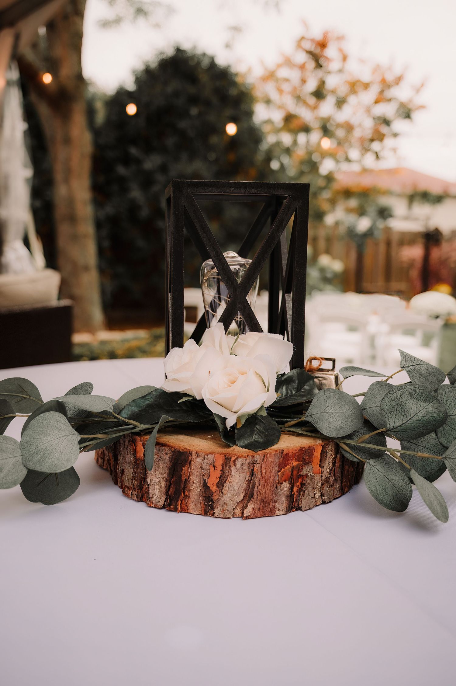 Rustic wedding table decor with wooden log slices and eucalyptus leaves on white tablecloth.