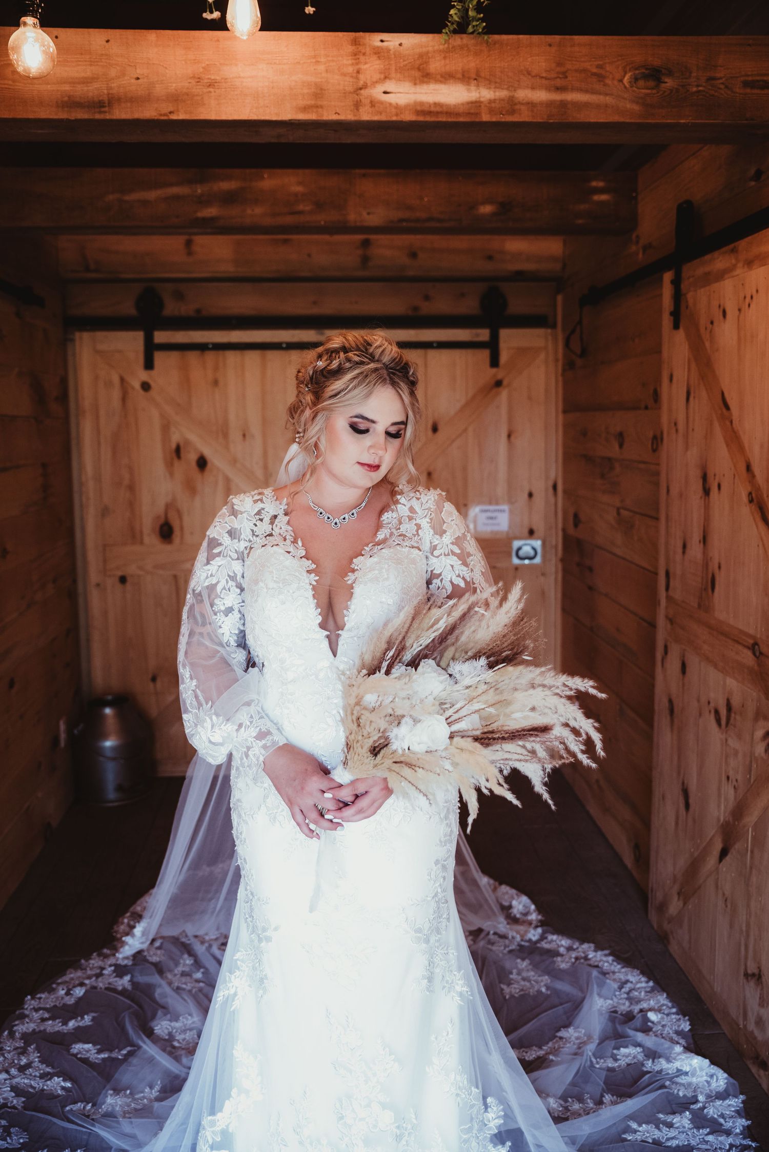 Bride in lace wedding dress with long sleeves sits in rustic wooden room.