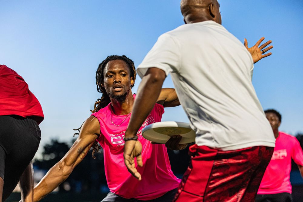 Athletes in pink jerseys compete in an intense ultimate frisbee game outdoors under a clear blue sky.