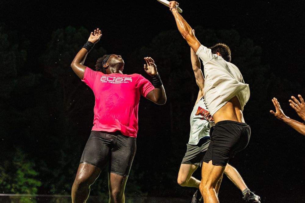 Two athletes compete for a disc in an intense nighttime ultimate frisbee game, one in a pink jersey.