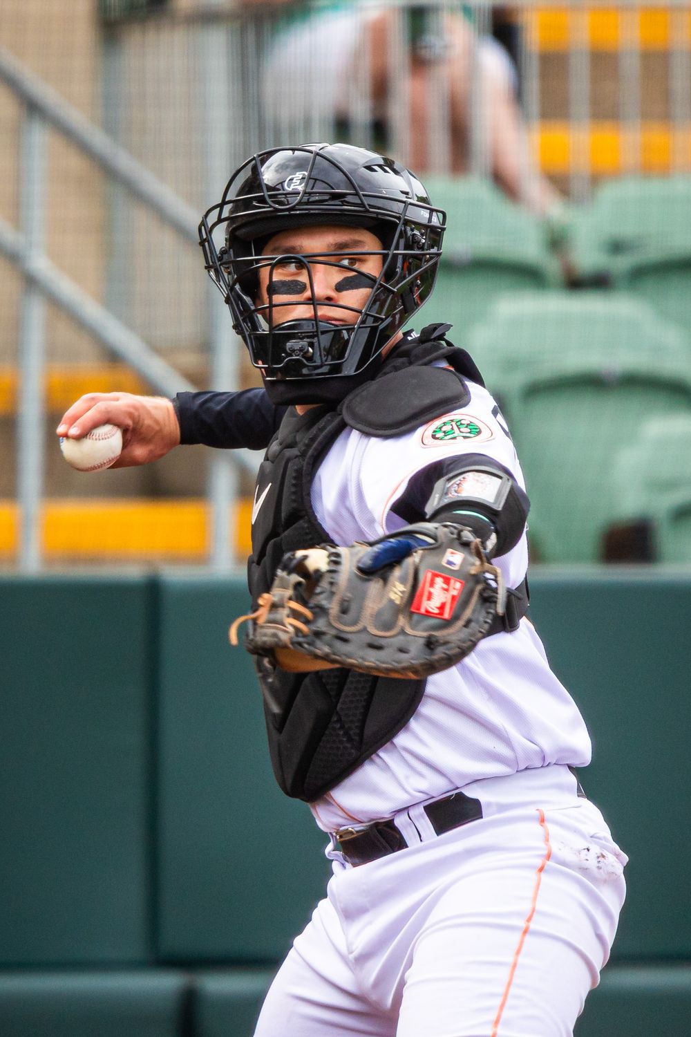 Baseball catcher in full gear, including helmet and chest protector, preparing to throw the ball during a game.