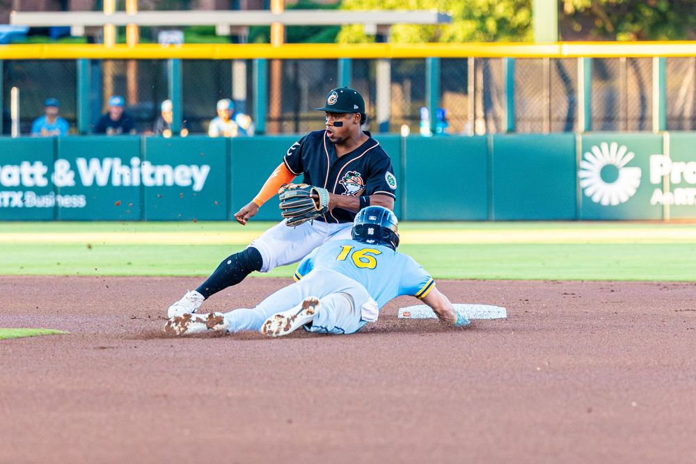 Baseball player sliding into second base as infielder attempts tag during minor league game.