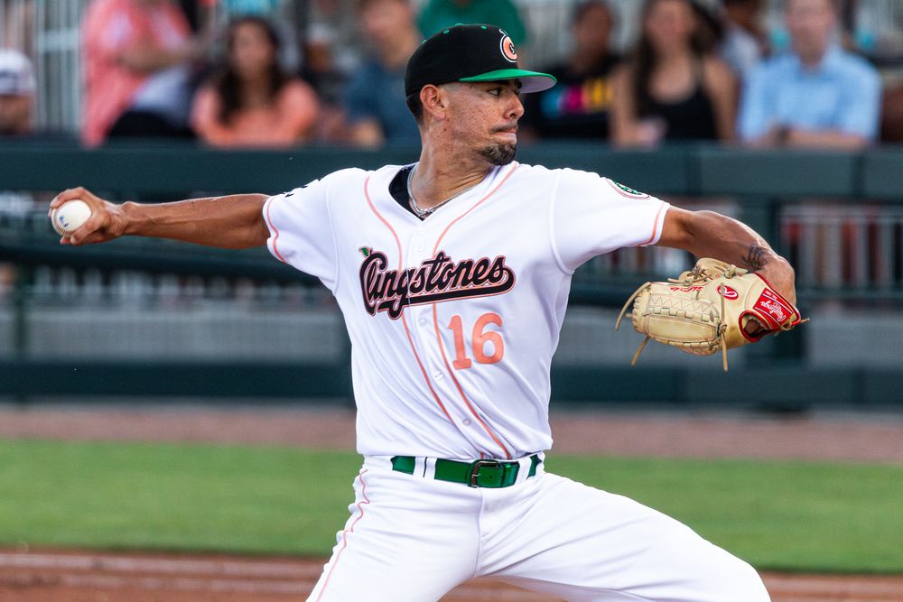 Professional baseball pitcher in white Capitales uniform winds up to throw during game at stadium.