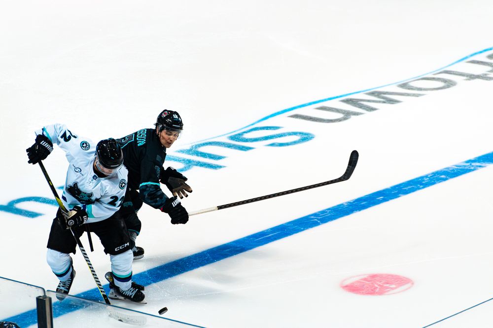 Two hockey players battle for position during a match on an ice rink with blue line markings.