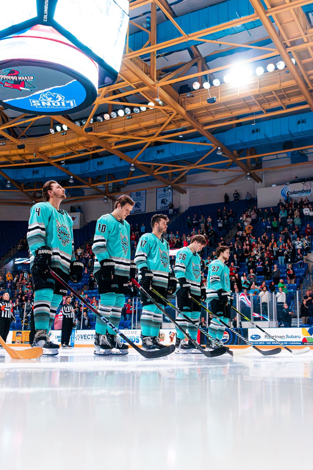 Hockey players in teal uniforms stand together during pre-game ceremony at an indoor arena.