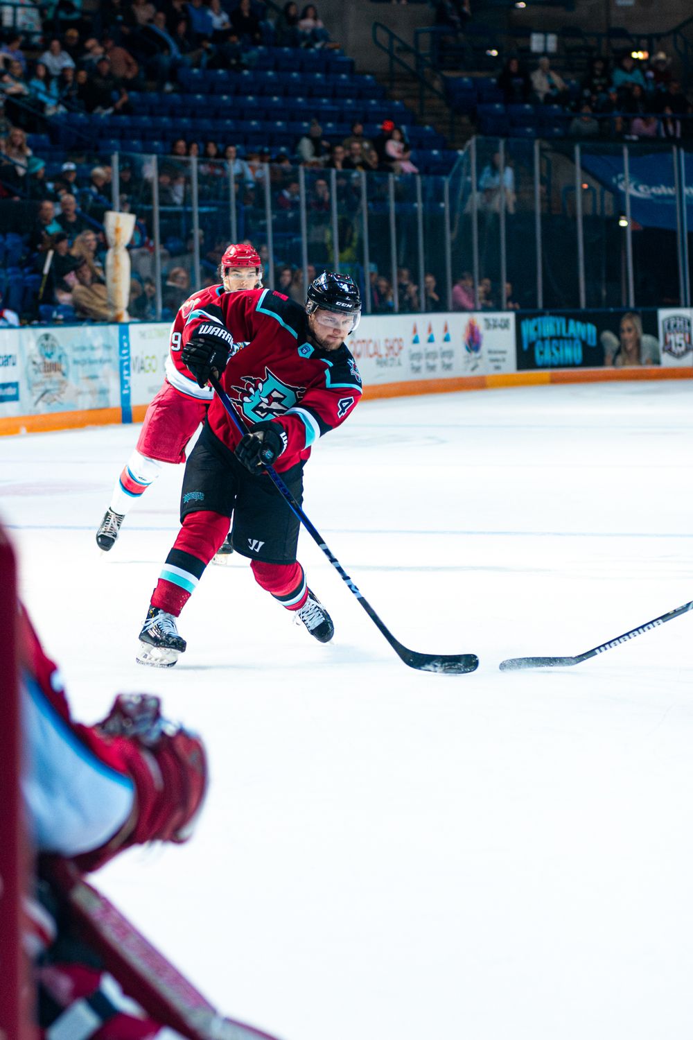 Ice hockey player in red jersey takes a shot during competitive game at indoor arena with spectators.