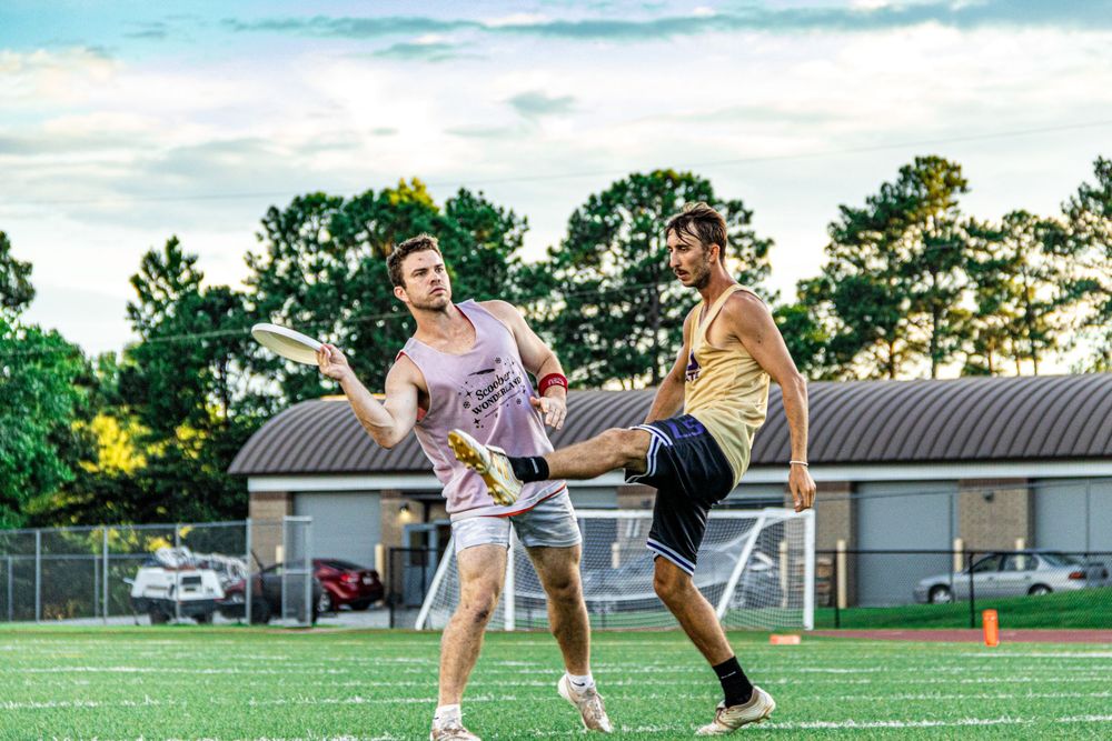 Athletes clash while playing ultimate frisbee on a grassy field during a sunny evening practice session.