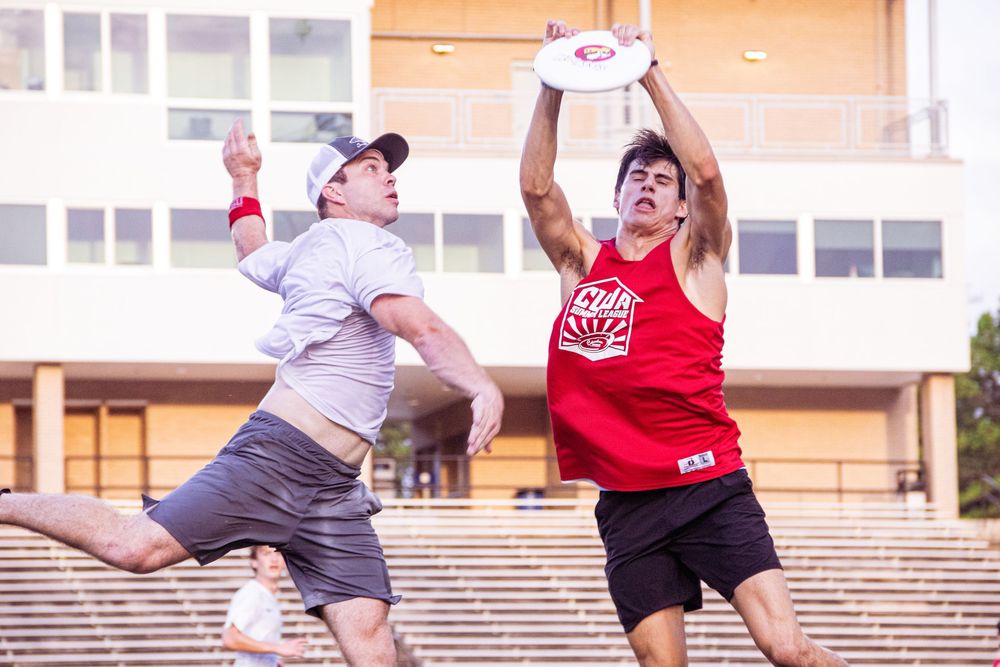 Two ultimate frisbee players compete for a catch during an intense match, one leaping to make a defensive play.