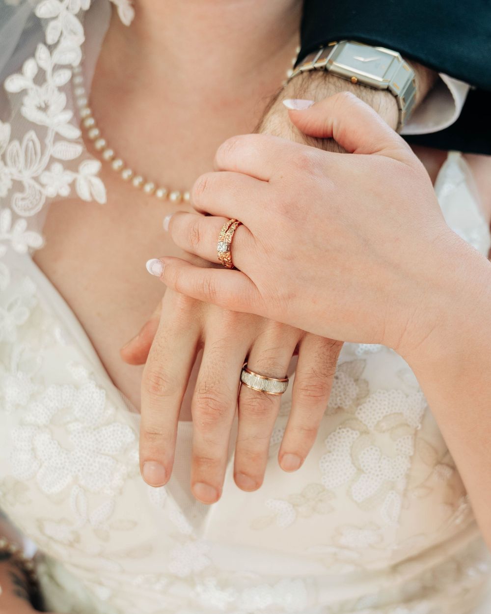 A series of elegant close-up shots showing hands with wedding rings against white lace and floral details.