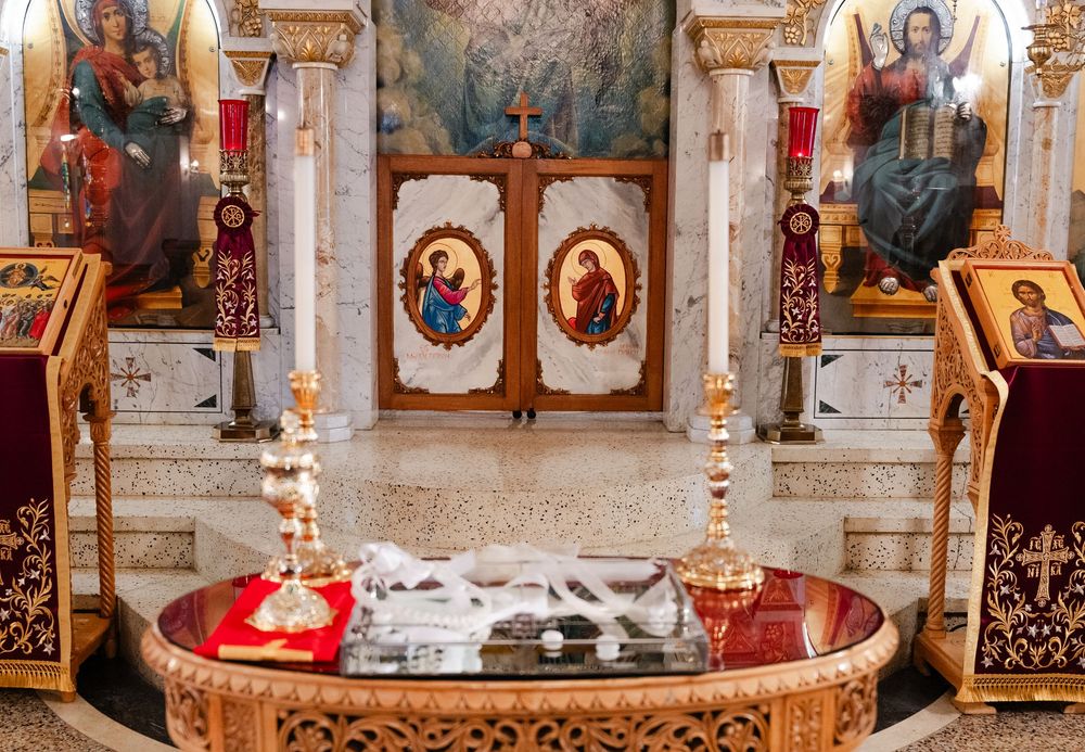 Interior view of an ornate Orthodox church showing gilded icons, candles, and religious artwork on the walls.