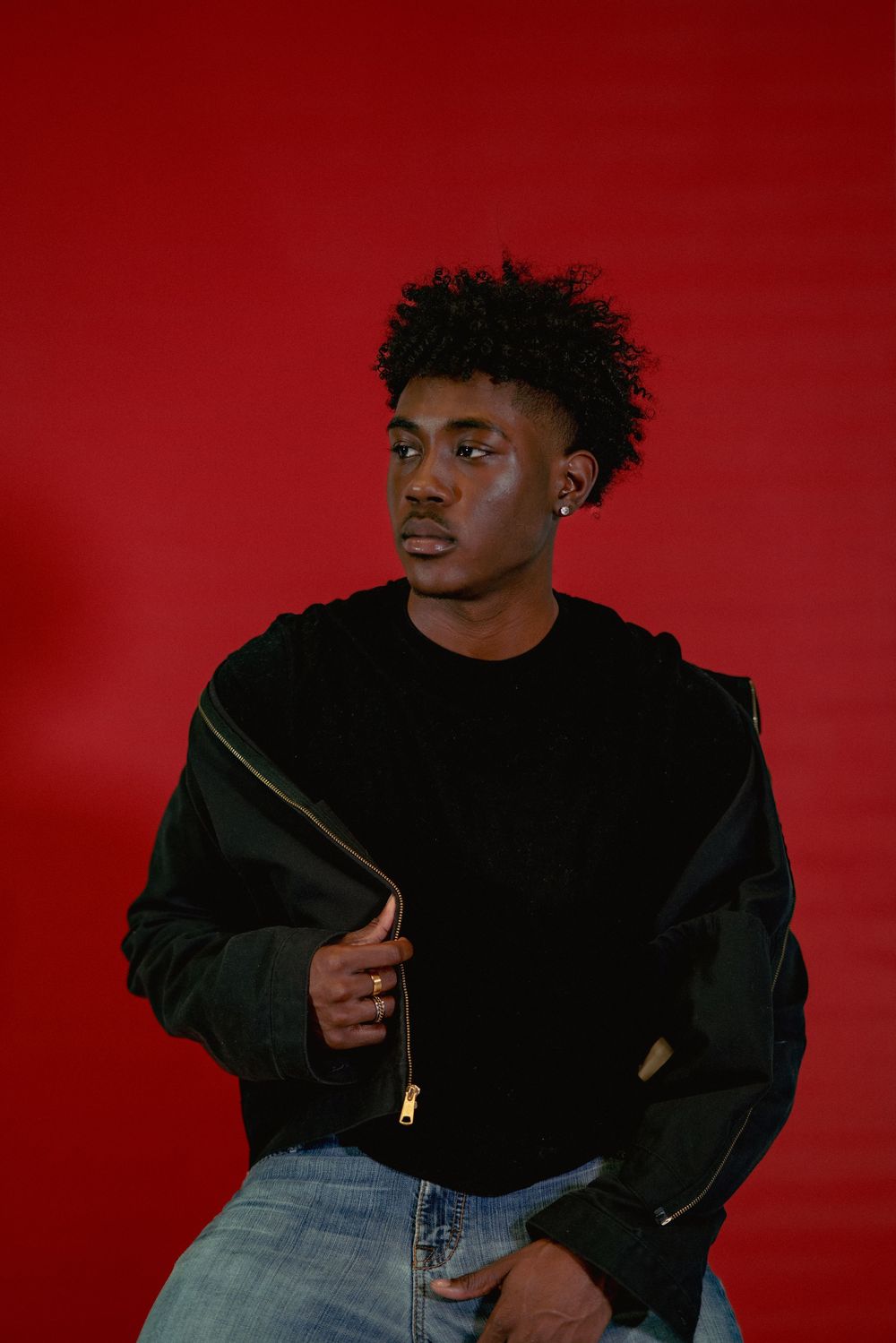 Portrait of a person in black hoodie against red background looking to the side in thoughtful pose.