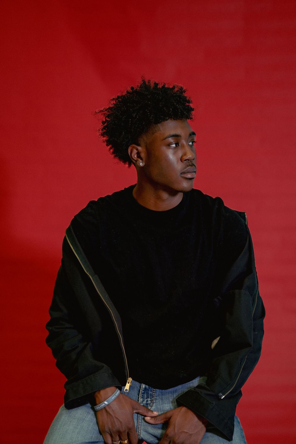 Portrait of someone in a black sweatshirt looking sideways against a red backdrop.