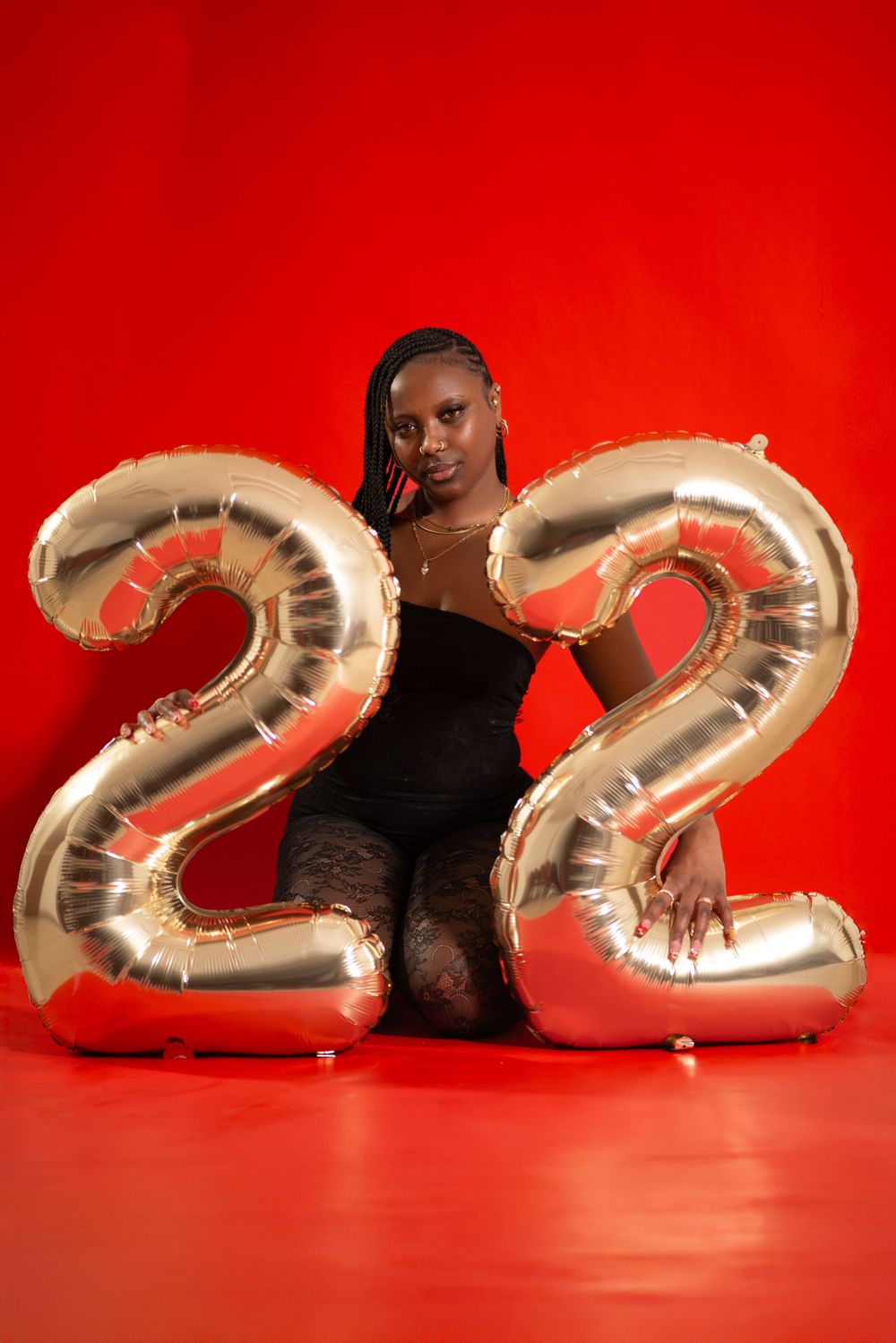 Someone posing with large silver inflatable number 22 balloons against a vivid red background.