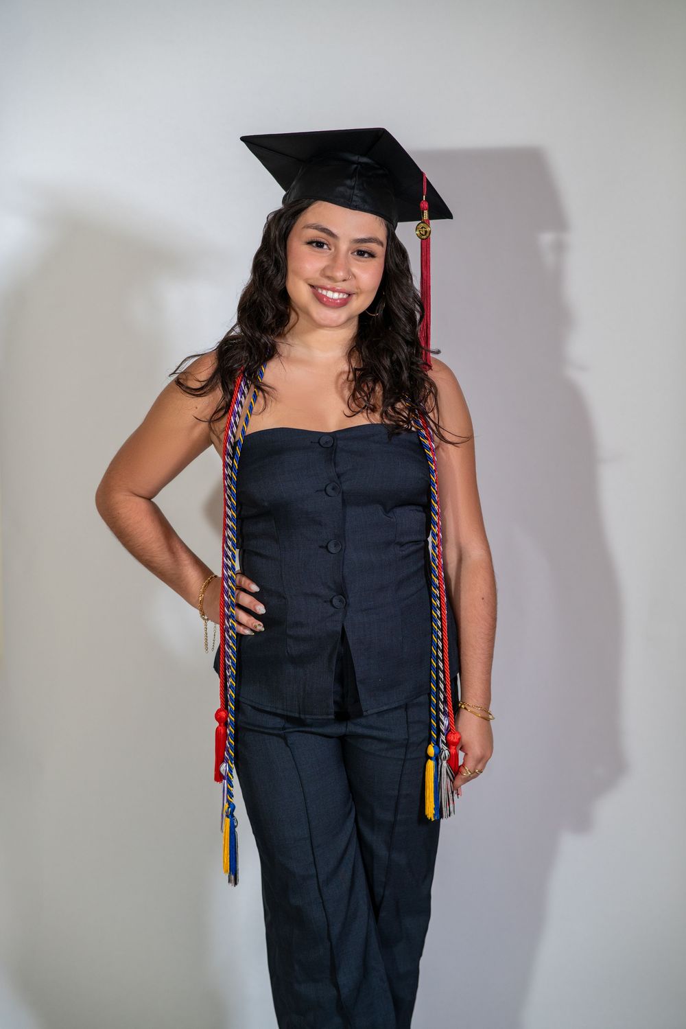 Graduate wearing black cap and gown with red and gold honor cords poses against white background.