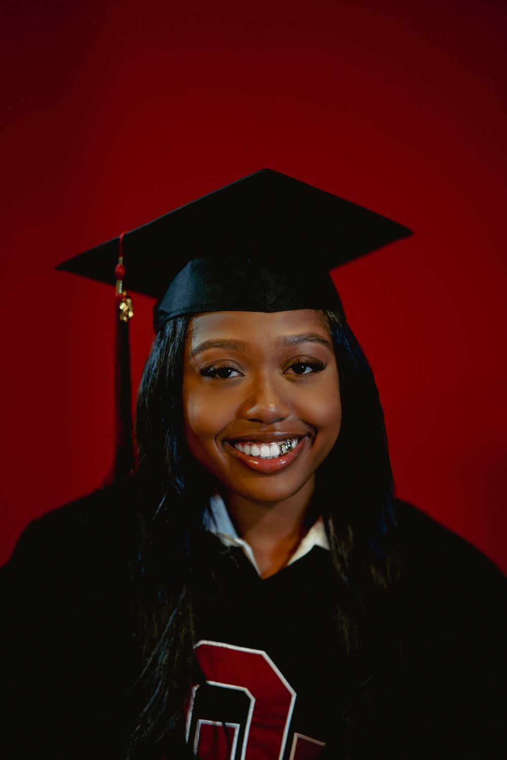 Graduate in black cap and gown wearing academic regalia against a deep red background.