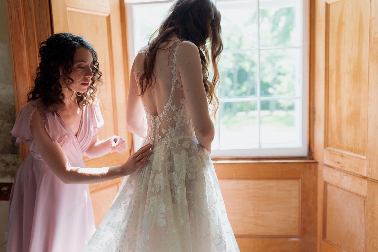 Wedding dress preparation scene with natural window light in historic room.