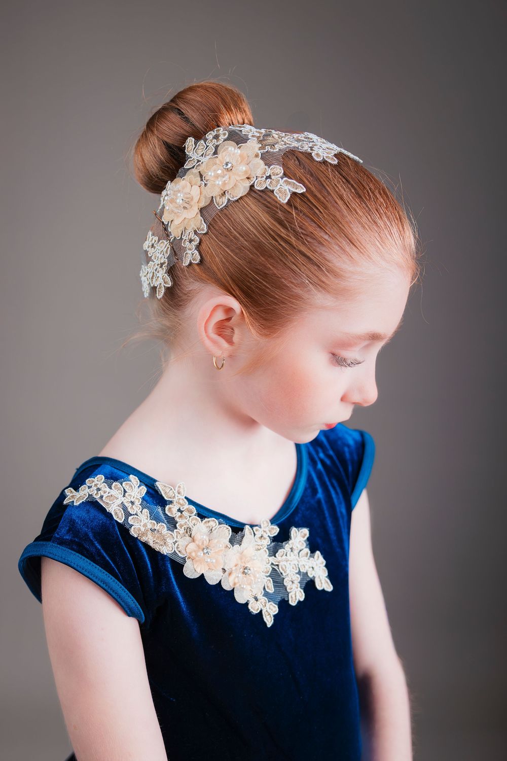 Young dancer wearing a royal blue velvet leotard with lace trim and an elegant floral hair accessory.